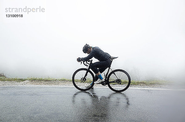 Mann entspannt sich auf dem Fahrrad auf nasser Straße bei nebligem Wetter