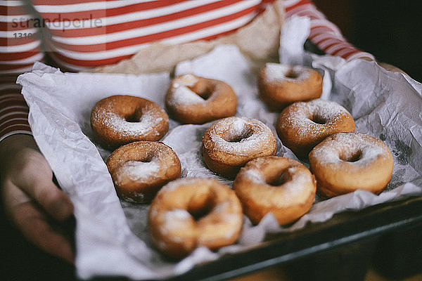 Mittelteil einer Frau  die zu Hause Donuts in einem Tablett hält