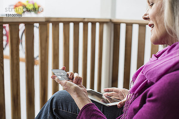 Nahaufnahme einer Frau  die bei der Benutzung eines Tablet-Computers auf ihre Kreditkarte schaut