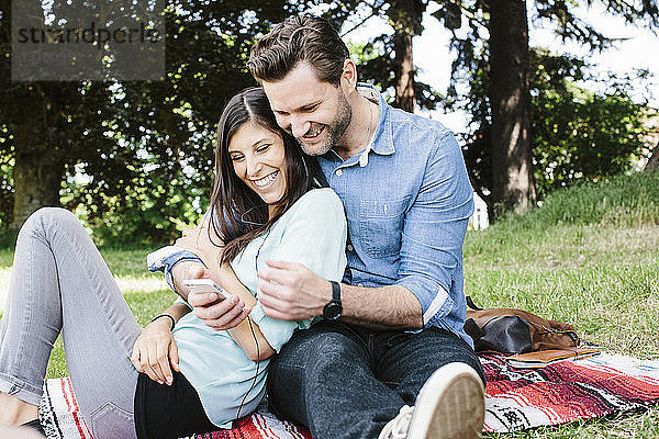 Glückliches Paar telefoniert im Park sitzend per Handy