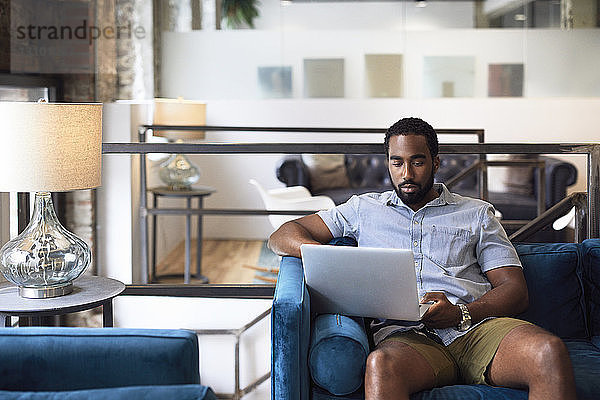 Geschäftsmann mit Laptop auf dem Sofa sitzend am Lampenschirm im Kreativbüro