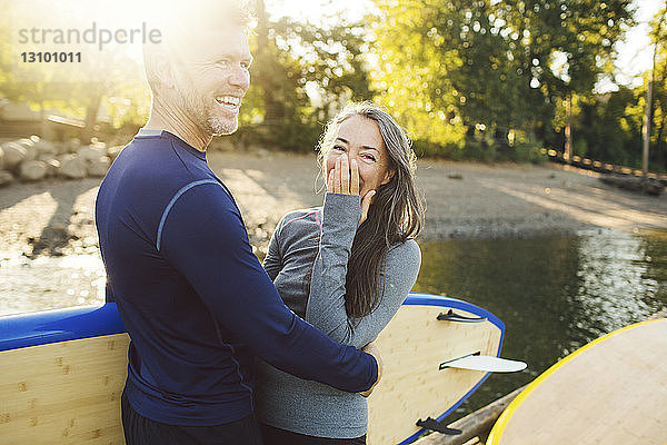 Glückliches Paar mit Paddelbrettern am Flussufer stehend