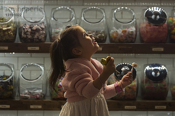 Seitenansicht eines glücklichen Mädchens mit Bonbons in der Hand  während es im Laden steht