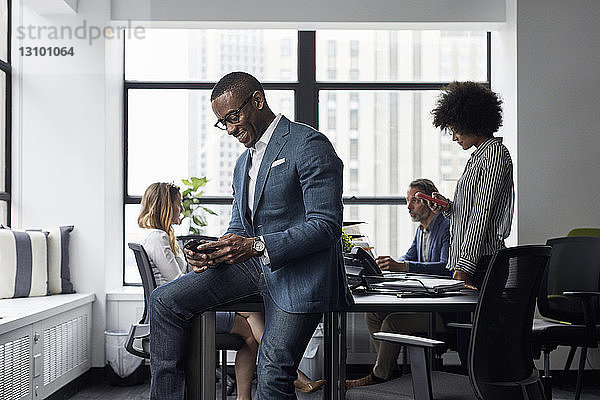 Geschäftsmann und Geschäftsfrau benutzen Smartphones  während ihre Kollegen im Büro arbeiten