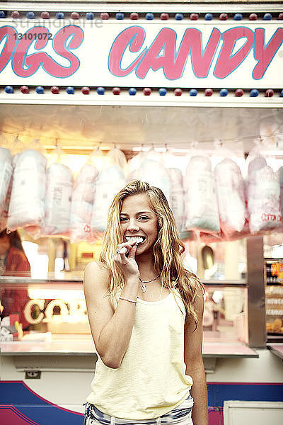 Porträt einer glücklichen Frau  die Zuckerwatte an einem Stand im Vergnügungspark isst