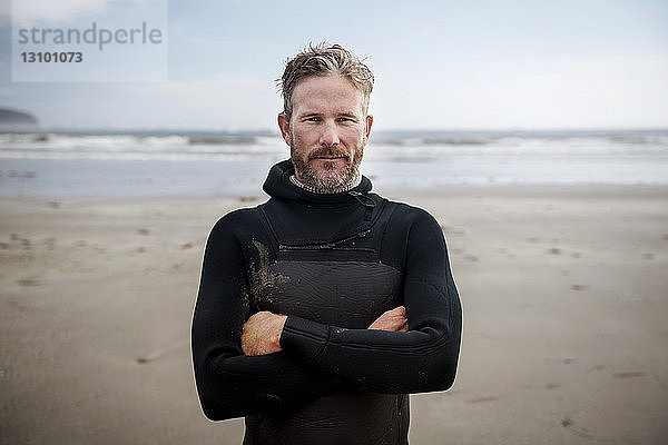 Porträt eines reifen Surfers  der mit verschränkten Armen am Strand steht