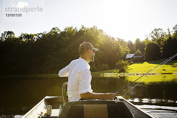 Mann angelt  während er bei Sonnenschein im Ruderboot auf dem See sitzt
