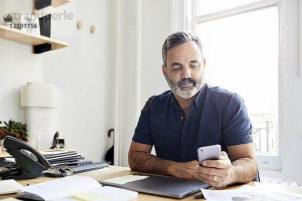 Geschäftsmann nutzt Smartphone  während er am Schreibtisch im Kreativbüro sitzt