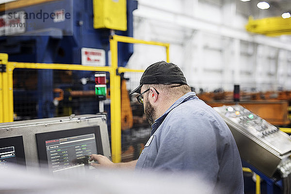 Seitenansicht eines Arbeiters  der eine Maschine bei der Arbeit in einem Metall-Stahlwerk benutzt