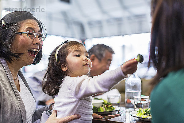 Mädchen  das seine Mutter füttert  während es mit den Großeltern am Tisch im Restaurant sitzt