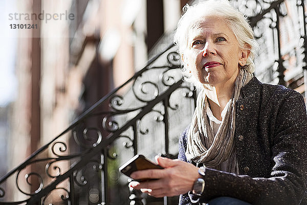 Nachdenkliche ältere Frau hält Smartphone im Freien