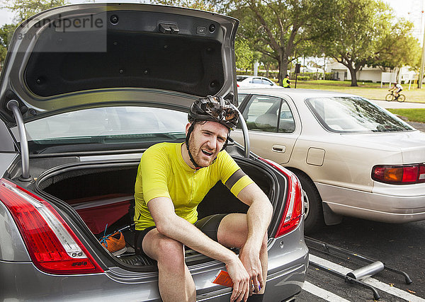 Müde männlicher Radfahrer sitzt im Kofferraum