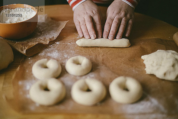 Abgehackte Hände einer Frau  die zu Hause in der Küche auf einem Holztisch Donuts zubereitet