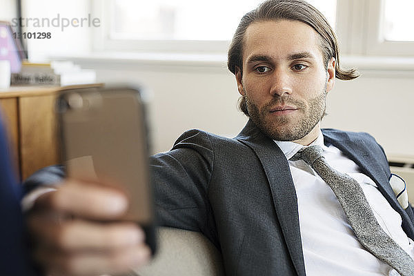 Geschäftsmann benutzt Mobiltelefon  während er zu Hause auf dem Sofa sitzt