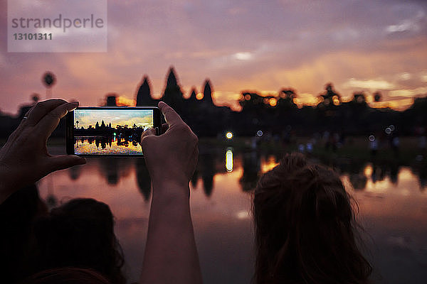 Ausschnitt eines Touristen  der die Silhouette des Tempels Angkor Wat bei Sonnenuntergang fotografiert