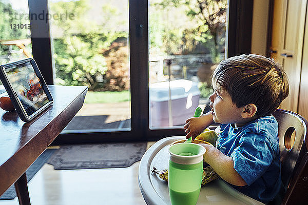 Junge schaut auf digitale Tablette und isst zu Hause