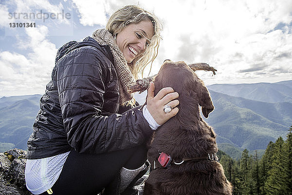 Niedrigwinkelansicht einer glücklichen Frau  die mit einem Hund auf einem Bergfelsen spielt