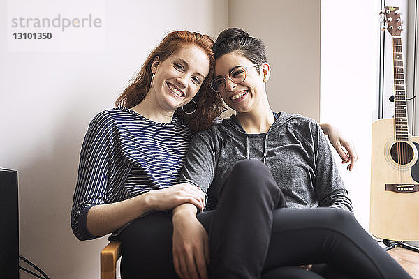 Glückliches lesbisches Paar sitzt zu Hause auf einem Stuhl