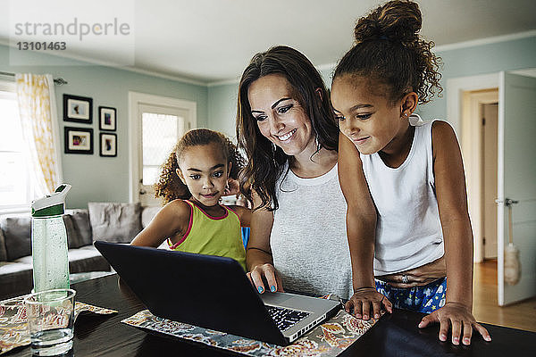 Glückliche Frau benutzt Laptop mit Töchtern zu Hause