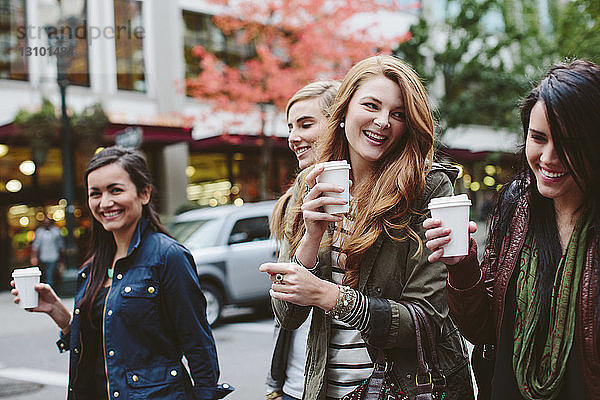 Fröhliche Freundinnen trinken Kaffee beim Spaziergang auf der Straße