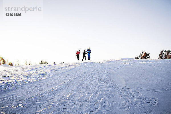 Freunde genießen auf schneebedecktem Berg vor klarem Himmel