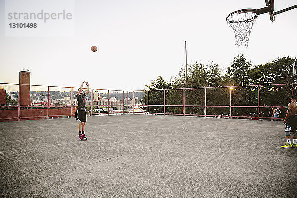 Freunde üben Basketball auf dem Platz gegen den klaren Himmel