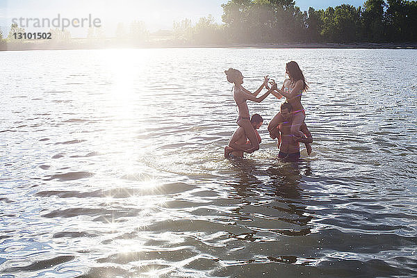 Männliche Freunde tragen Frauen auf den Schultern  während sie sich im Fluss vergnügen