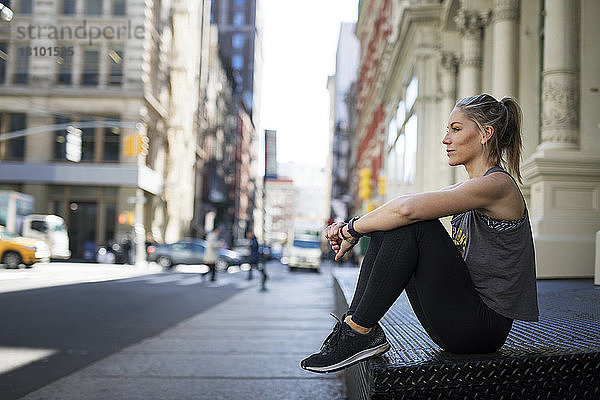 Nachdenklicher Sportler entspannt sich auf dem Bürgersteig in der Stadt