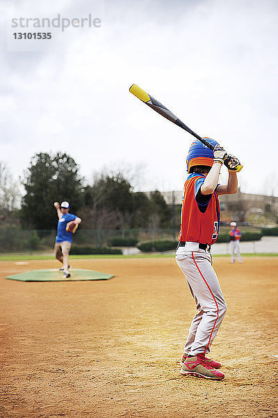 Seitenansicht eines Baseball spielenden Jungen mit Trainer auf dem Feld gegen den Himmel