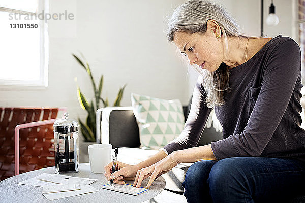 Konzentrierte Frau schreibt am Tisch im Wohnzimmer auf Papier