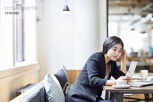 Glückliche Geschäftsfrau benutzt Smartphone  während sie im Büro am Tisch sitzt