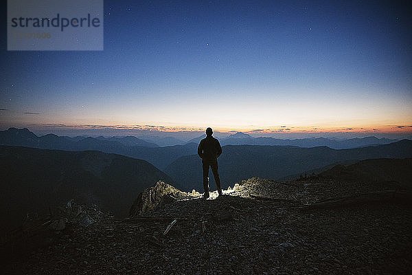 Rückansicht eines Mannes  der bei Sonnenuntergang auf einem Berg gegen den Himmel steht
