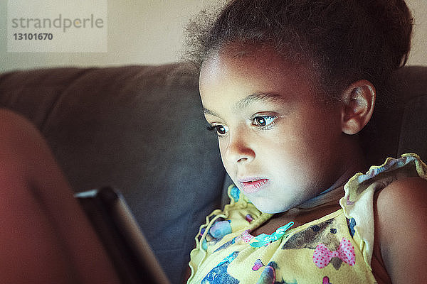 Nahaufnahme eines Mädchens  das einen Tablet-Computer benutzt  während es zu Hause auf dem Sofa sitzt