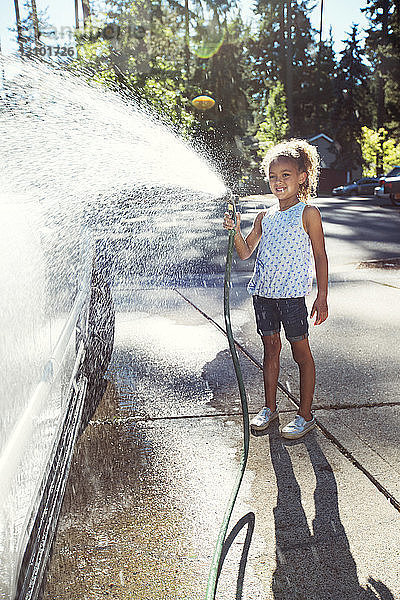 Mädchen sprüht Wasser auf Auto in Einfahrt