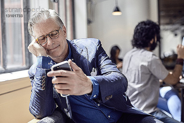 Geschäftsmann betrachtet Smartphone mit einem männlichen Kollegen im Hintergrund