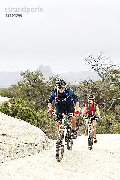 Lächelndes Paar fährt Fahrrad auf Felsen gegen klaren Himmel
