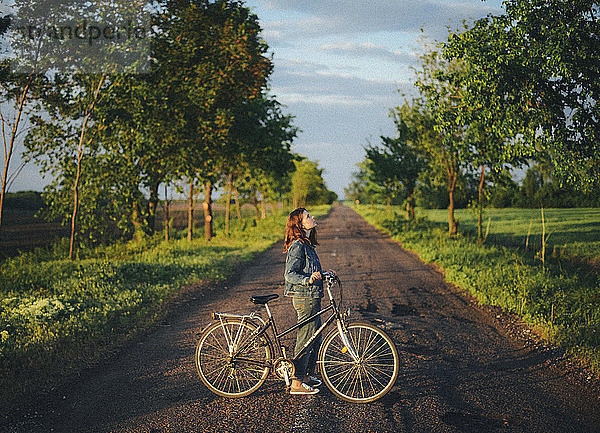 Seitenansicht einer Frau mit Fahrrad  die bei Sonnenuntergang auf der Straße gegen den Himmel steht