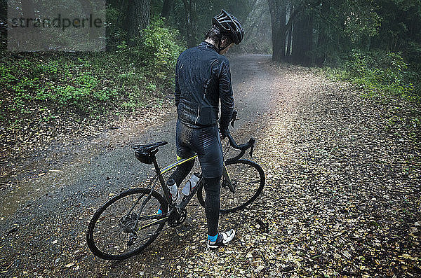 Hochwinkelaufnahme eines Mannes  der mit einem Fahrrad auf einem Feldweg im Wald steht