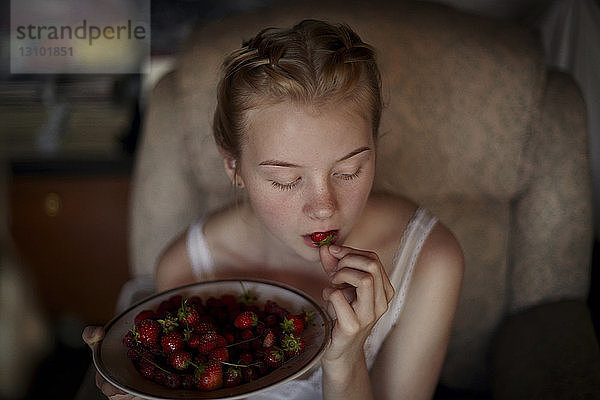 Hochwinkelaufnahme einer Frau  die zu Hause sitzend Erdbeeren isst