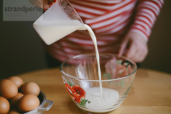 Mitschnitt einer Frau  die zu Hause auf einem Holztisch Milch in eine Schüssel gießt