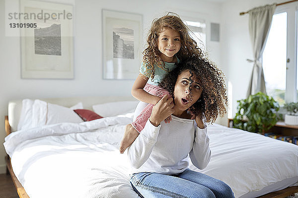 Porträt einer Tochter  die mit der Mutter spielt  die zu Hause auf dem Bett sitzt