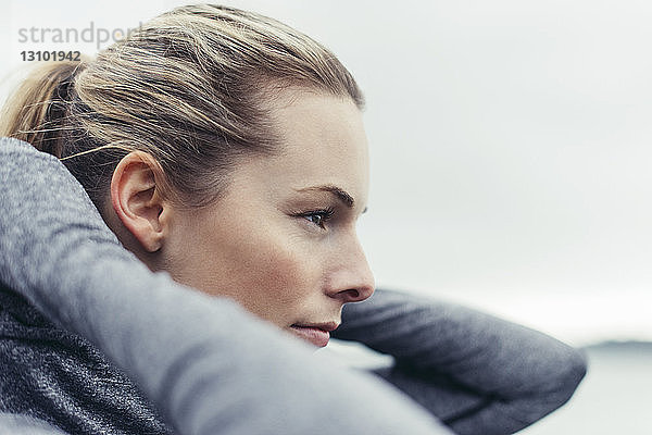 Nahaufnahme einer nachdenklichen  sportlichen Frau mit Kapuzenjacke vor klarem Himmel