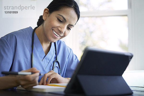 Lächelnde Ärztin schreibt während der Arbeit am Schreibtisch im Krankenhaus Tagebuch