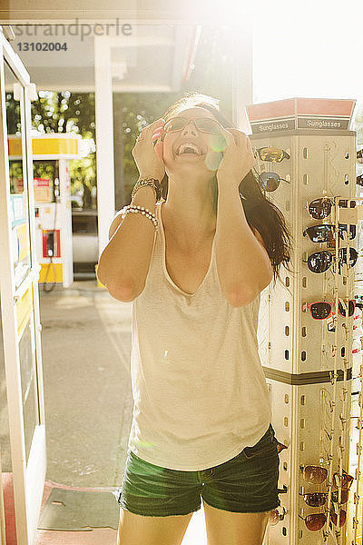 Fröhliche Frau probiert Sonnenbrille an der Tankstelle aus