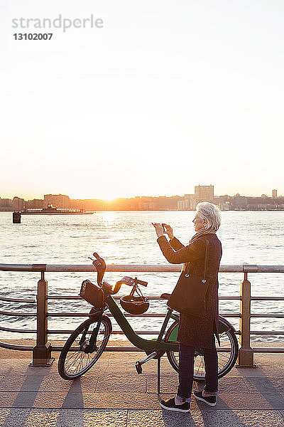 Ältere Frau in voller Länge fotografiert  während sie bei Sonnenuntergang auf der Promenade steht