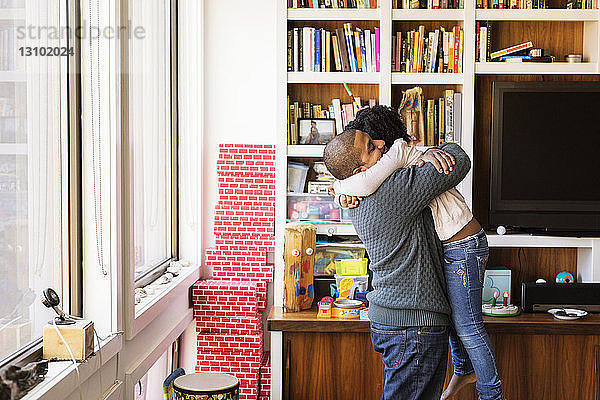 Seitenansicht eines Mannes  der seine Tochter umarmt  während er zu Hause steht