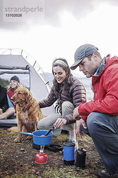 Freunde bereiten auf dem Campingplatz Essen mit Hund zu