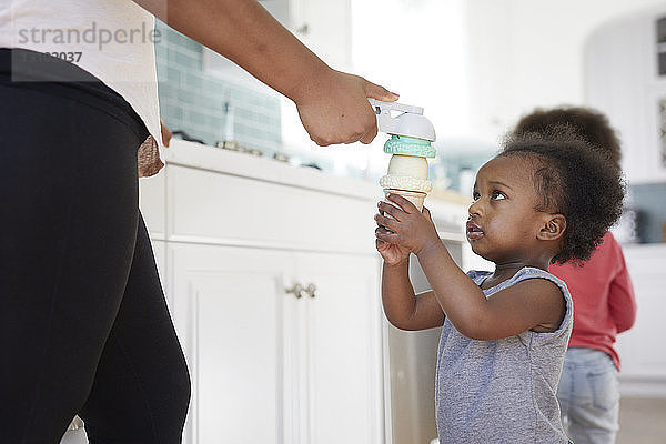 Mutter hält Eiscreme-Spielzeug in der Hand  während sie mit der Tochter zu Hause in der Küche spielt