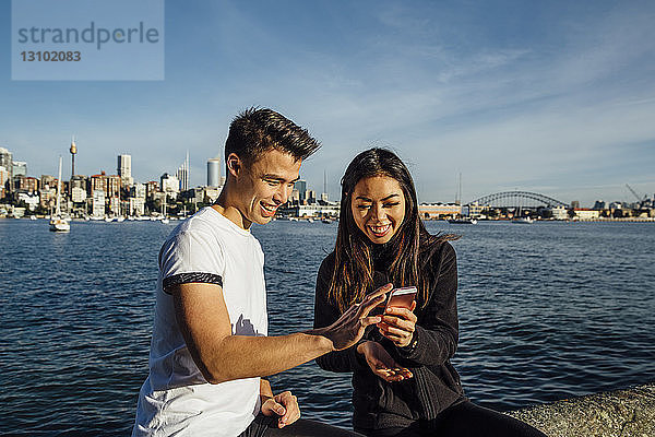 Glückliches junges Paar nutzt Smartphone beim Training auf der Promenade gegen die Sydney Harbour Bridge