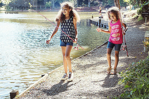 Mädchen tragen Angelruten beim Spaziergang am Seeufer